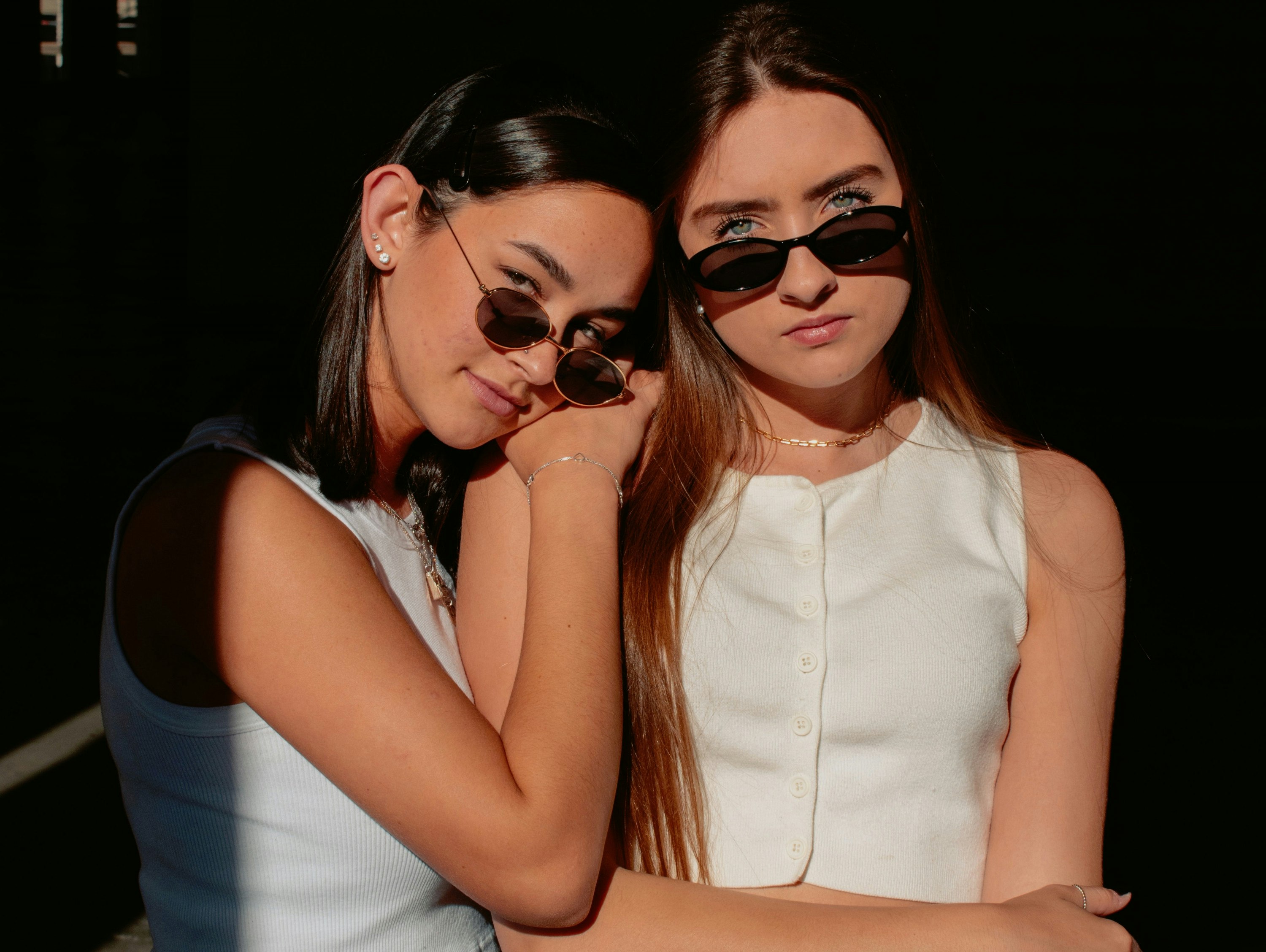 Two women lean on each other while soaked in sunshine.