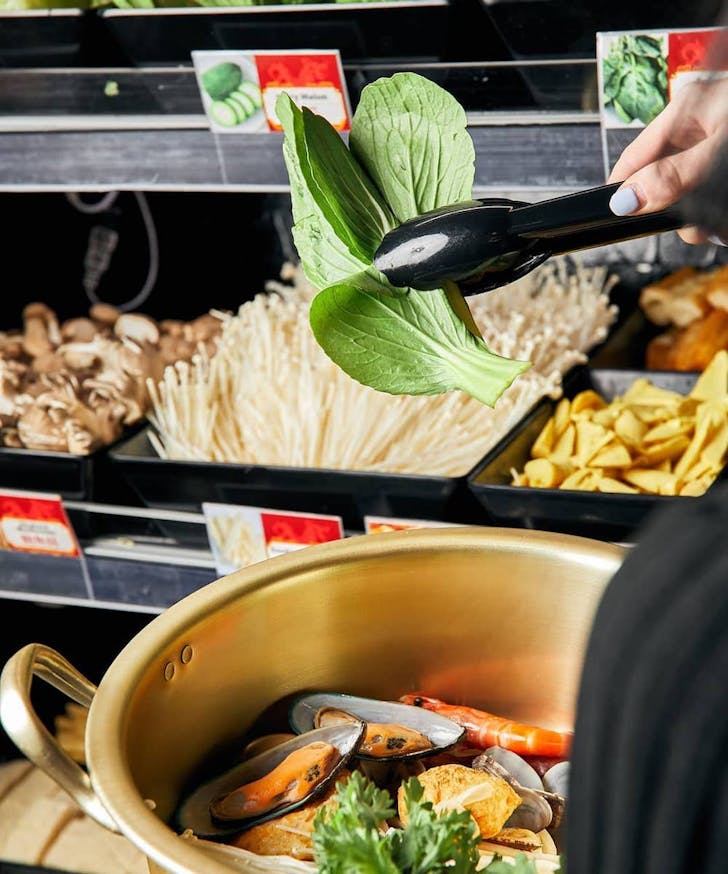 person putting produce into their hot pot