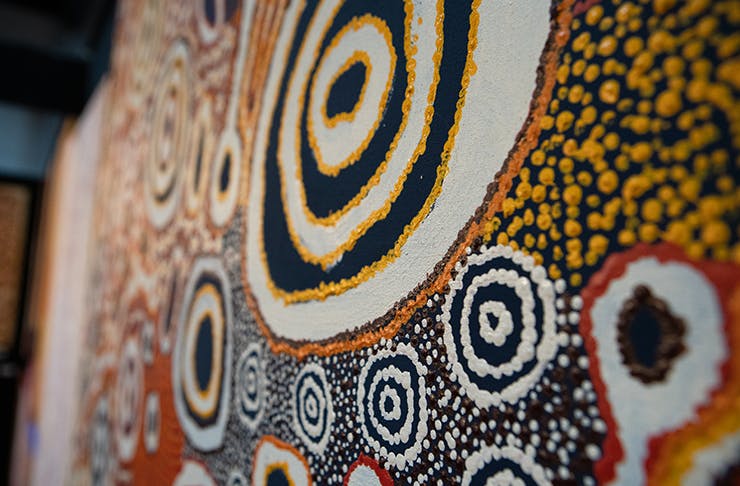 A traditional Aboriginal dot painting consisting of a large circle in the middle, which is surrounded by smaller, similar shapes.