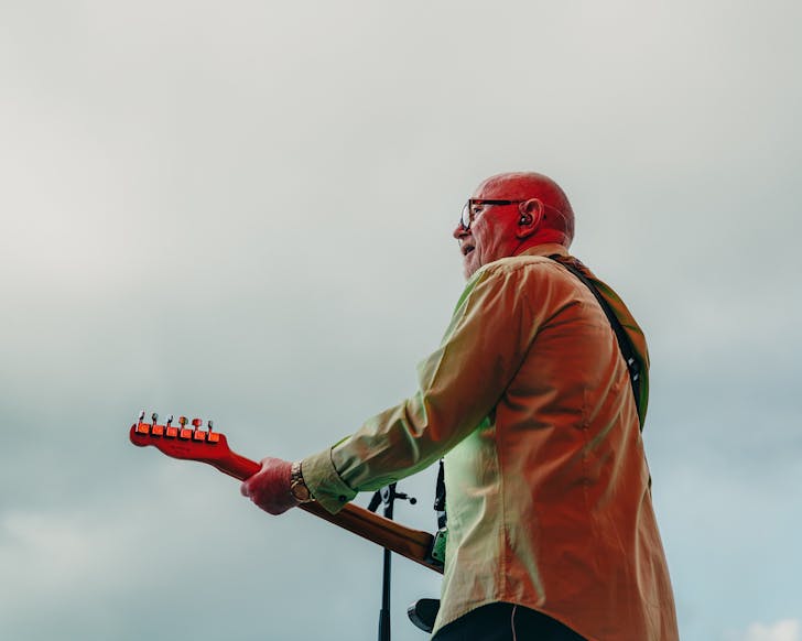 Dave Dobbyn plays his guitar onstage at an outdoor concert.