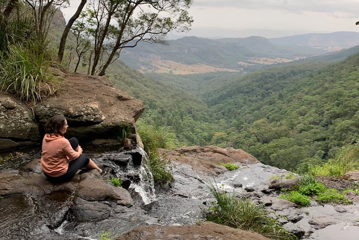 a person sitting at the top of a waterfall overlooking a valley