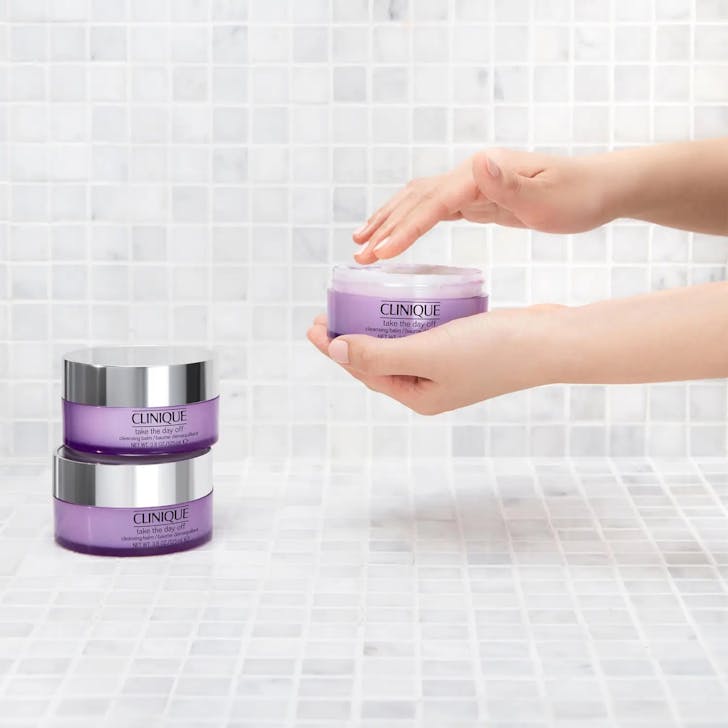 Womans hand using Clinique balm on tiled background