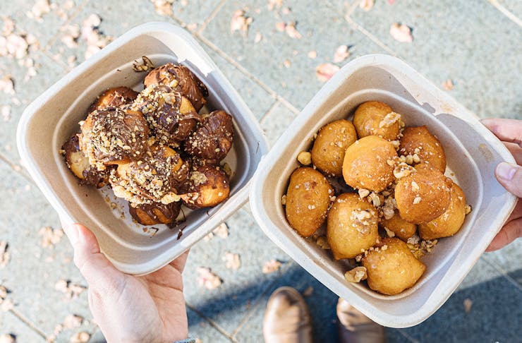 two takeaway boxes of loukoumades, one with nutella and one with honey and nuts