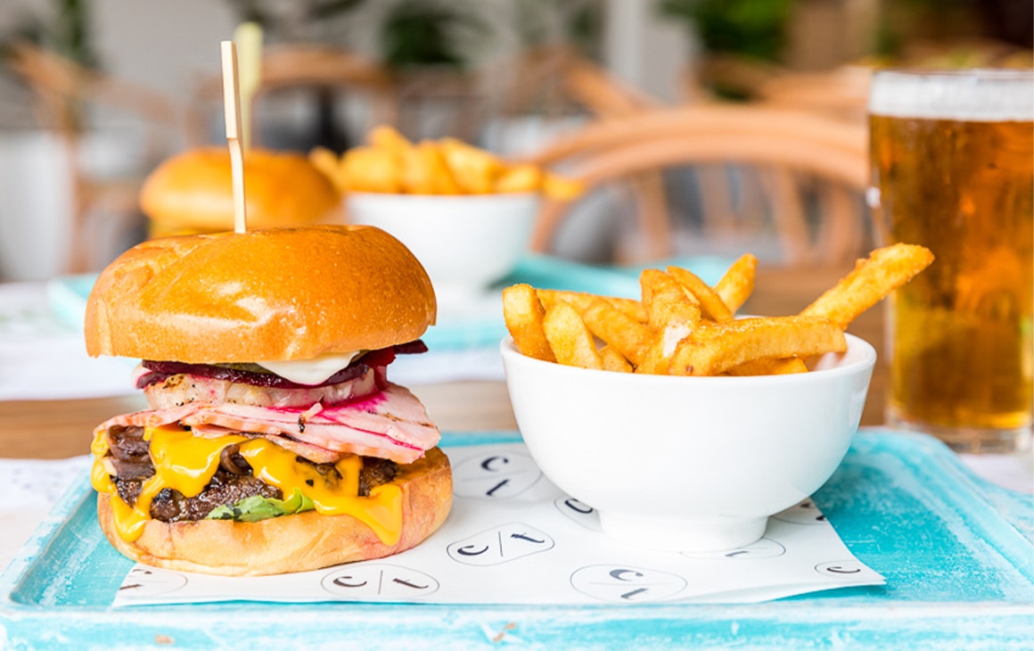 a burger and a bowl of chips on a tray with a pint of beer