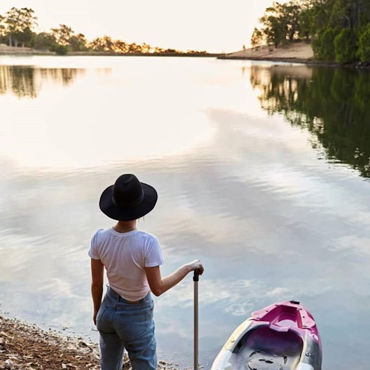 Woman stands next to a kayak at the edge of a lake in Ferguson Valley
