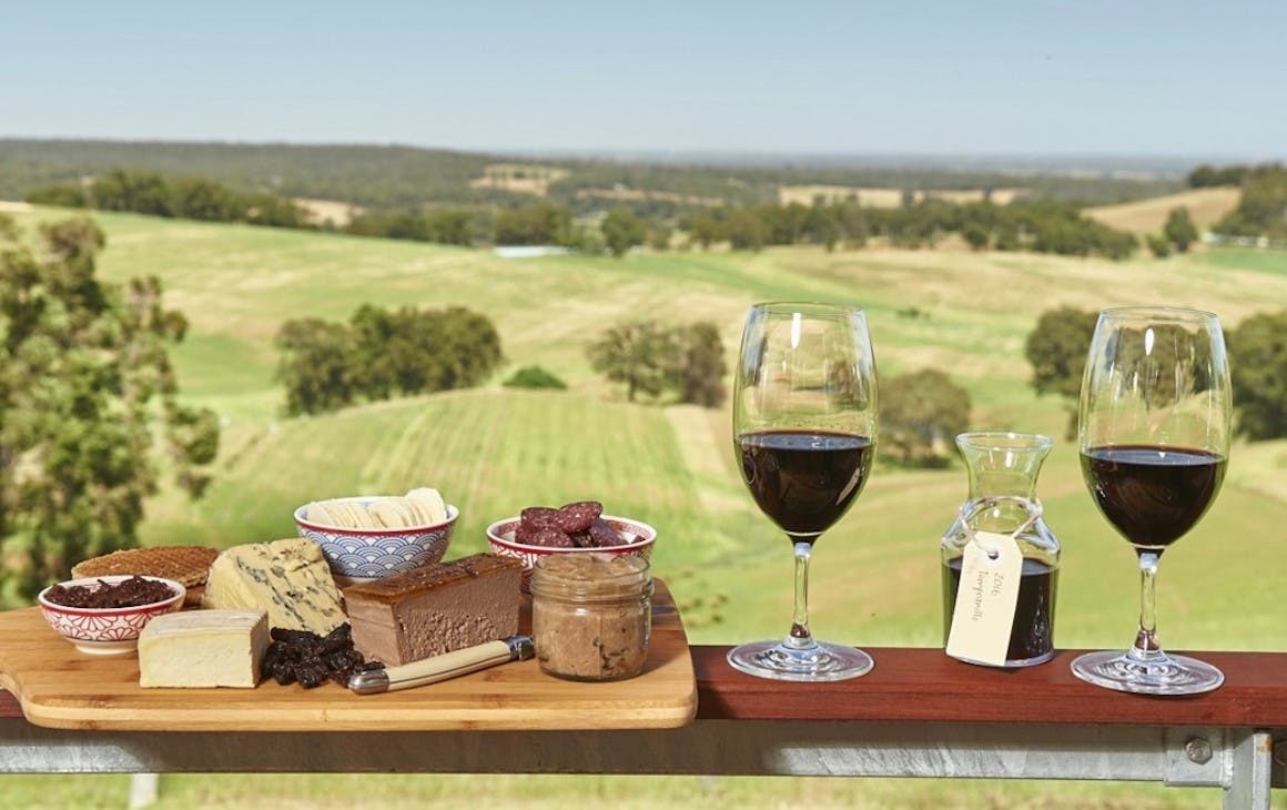 Things to do Ferguson Valley - two glasses of wine and a cheese board rest on balcony overlooking rolling green hills