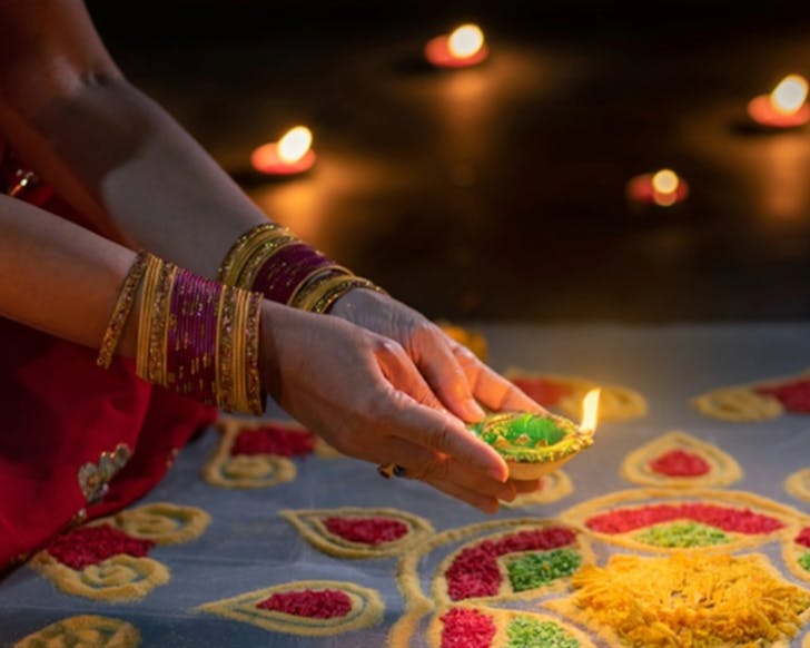 A close up photo of a lady placing down her oil candle for the diwali festival.
