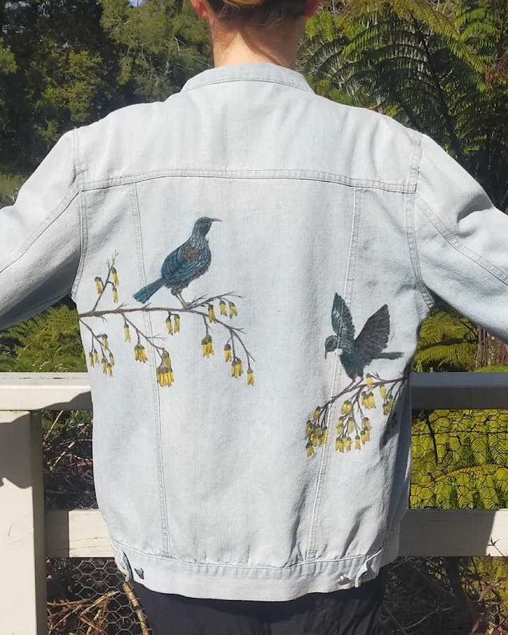 The back of someone wearing a DIY painted jacket featuring two tÅ«Ä«s on opposing branches.