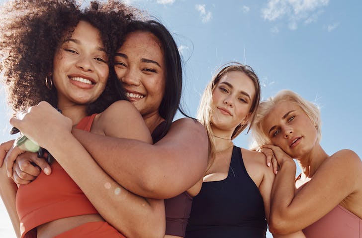 Four friends wear dk.active activewear and hug happily under a blue sky.