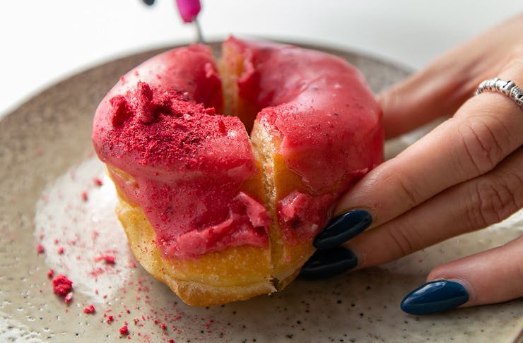 A person with blue nails cuts into a doughnut from donuts.
