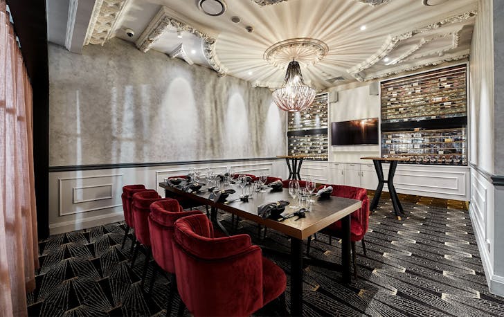 a white room with a chandelier above a glass table surrounded by red velvet chairs