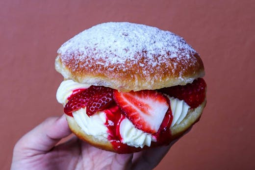 A hand holding up a strawberry and cream cheese doughnut.