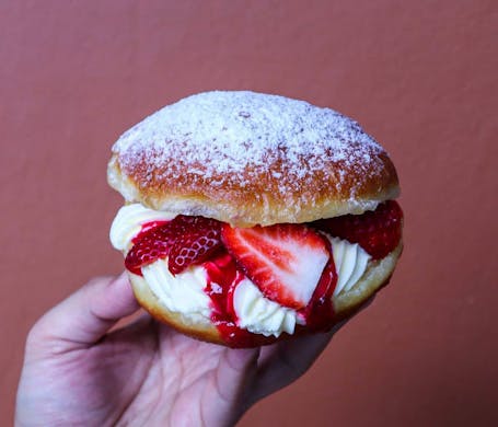 A hand holding up a strawberry and cream cheese doughnut. 