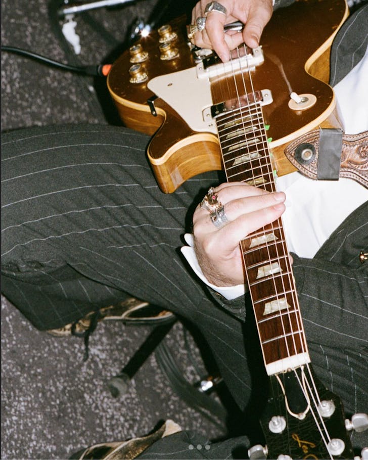 A close up flash image of Dope Lemon in a pin-striped suit playing his electric guitar.