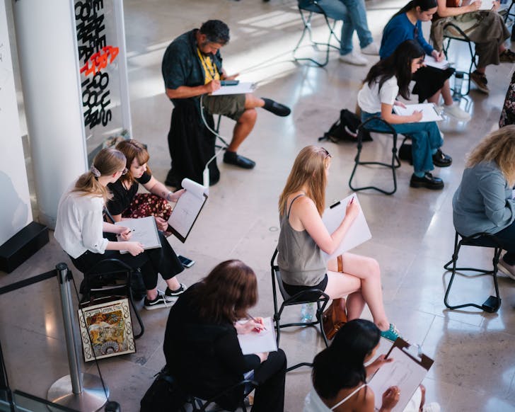 Bird's eye view of people sitting in an open, natural-light-filled space in Auckland Art Gallery for a drawing session.
