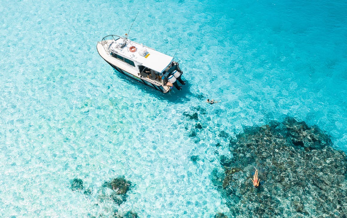 boat floating in crystal clear ocean over a reef