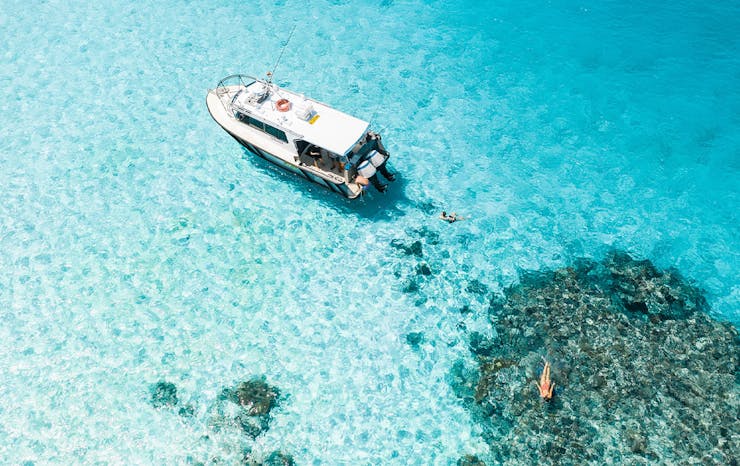 boat floating in crystal clear ocean over a reef