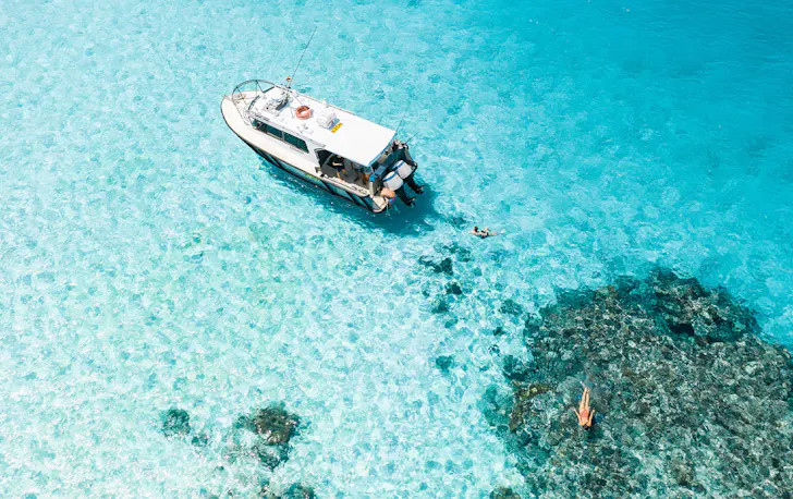 boat floating in crystal clear ocean over a reef