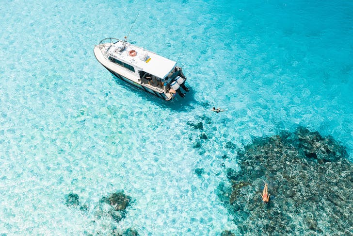 boat floating in crystal clear ocean over a reef