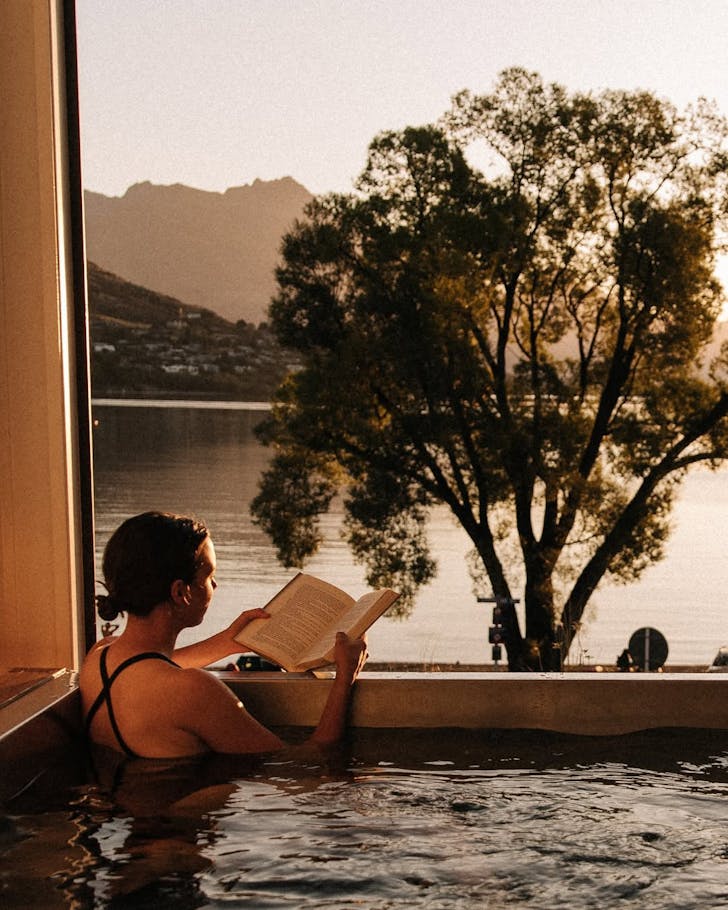 A woman reads at sunset while soaking in a hot pool at Driftaway holiday park
