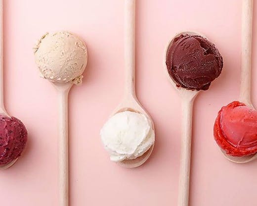 Four scoops of gelato, each sitting on a pink spoon in front of a pink background.
