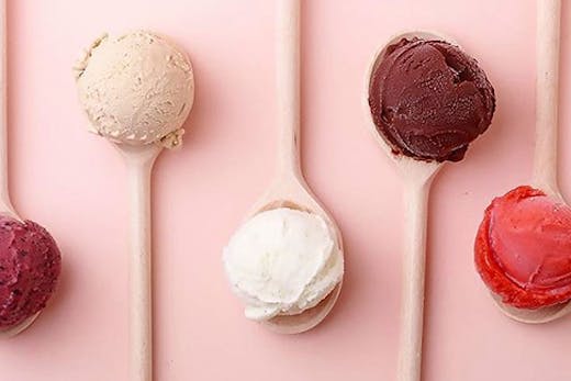 Four scoops of gelato, each sitting on a pink spoon in front of a pink background.