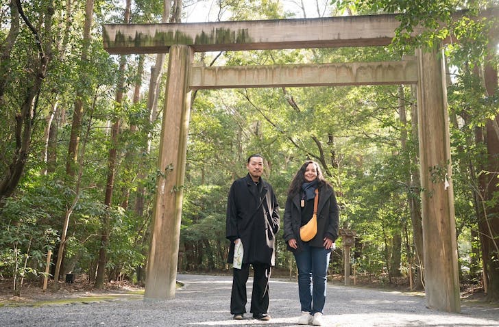 Brazilian-born artist Roberta Queiroga and Japanese master Junichi Ito stand in front of trees and a Japanese archway.