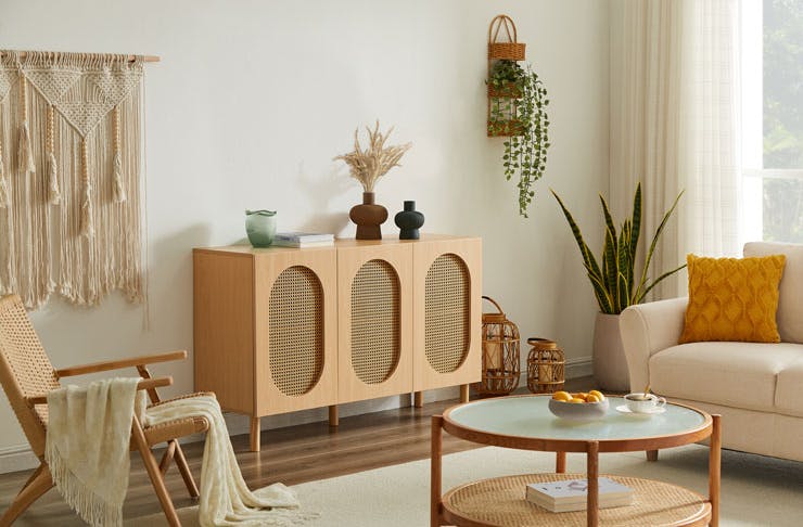 A boho-style living room, featuring a rattan sideboard, glass coffee table, and plus a white couch. 