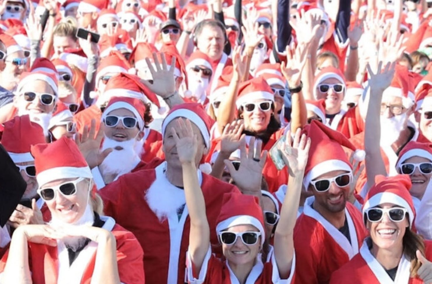 A crowd of people dressed as Santa and in sunglasses, ready for a morning run club run.