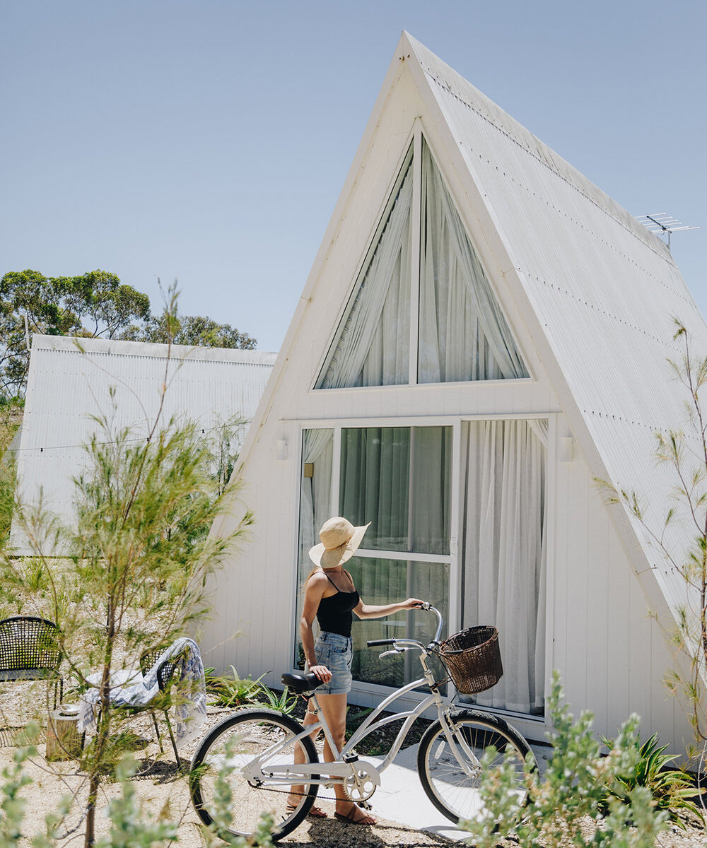 a women stands with a bike in front of an A-Frame chalet in Esperance