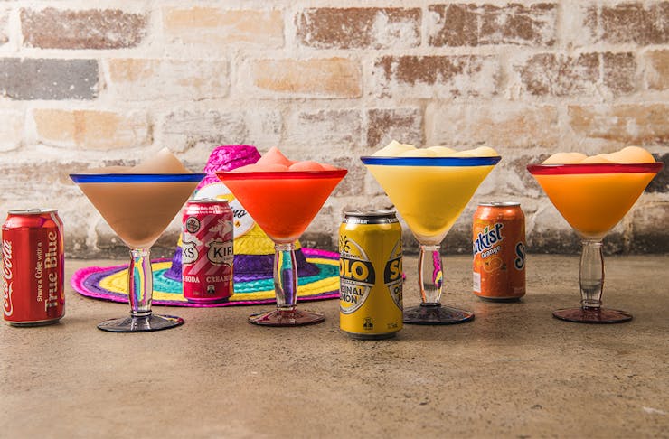 a row of frozen margaritas with soft drink cans alongside