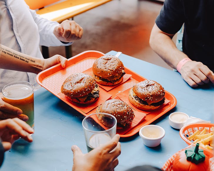 People sit at a table as burgers are delivered.