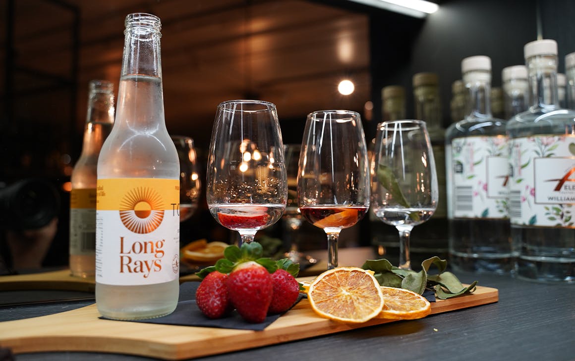 several gin glasses on a board with a bottle of tonic