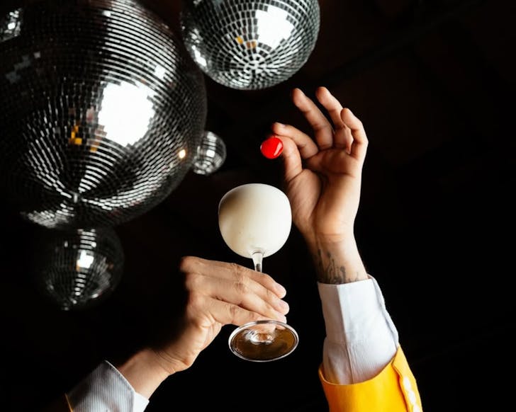 Disco balls above a bartender garnishing a banana daiquiri with a glacÃ© cherry