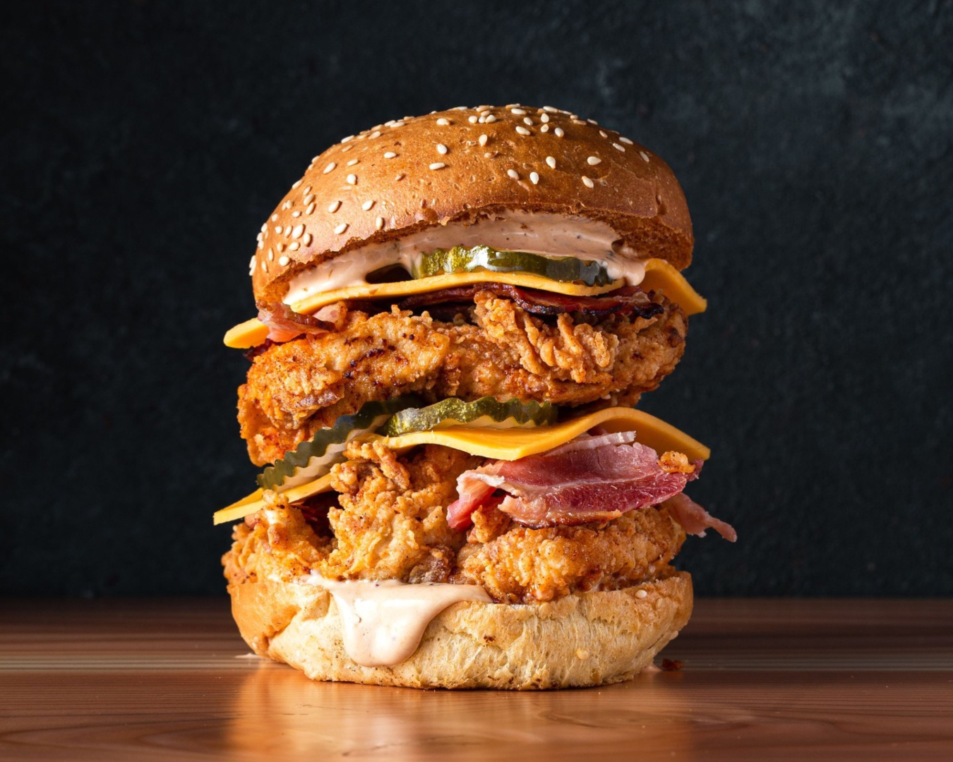 A crispy fried chicken burger from Empire Chicken is stacked high with cheese, pickles, and bacon