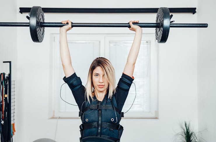 woman in an EMS training vest lifting a barbell