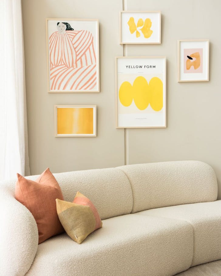 A curved cream sofa in front of a textured wall with various yellow-toned artworks.