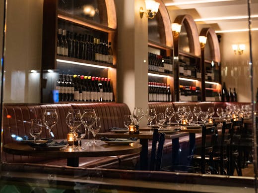 Red leather booths and tables set with wine glasses at Enoteca Ponti. 