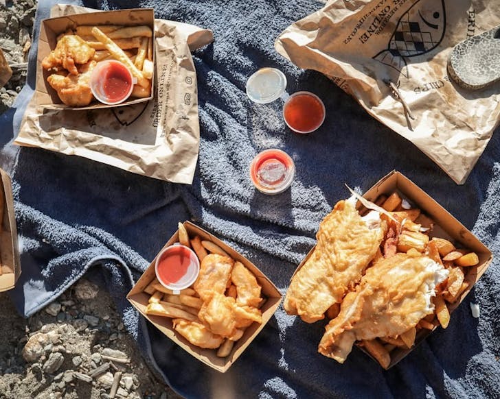 A picnic-style setting of fish and chips on the beach. 
