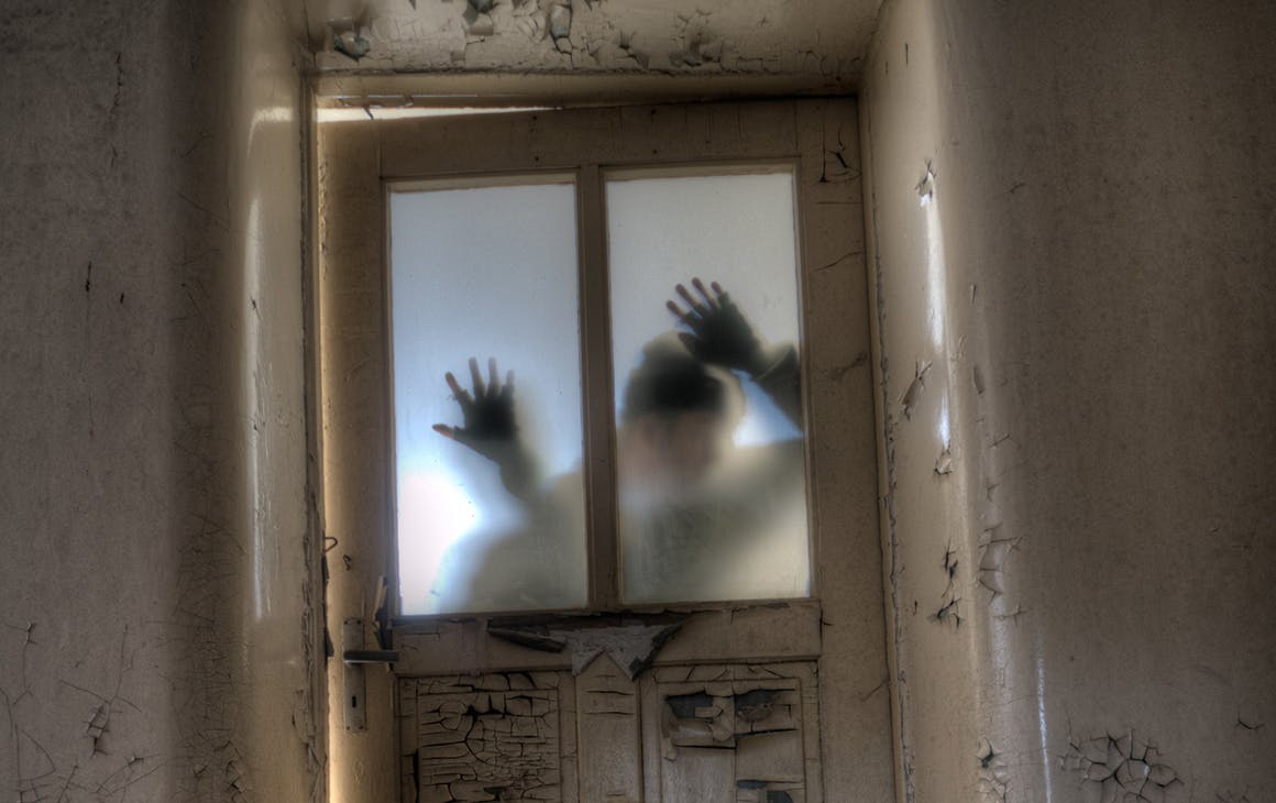 A man's shadow on a locked door with hands on the glass.