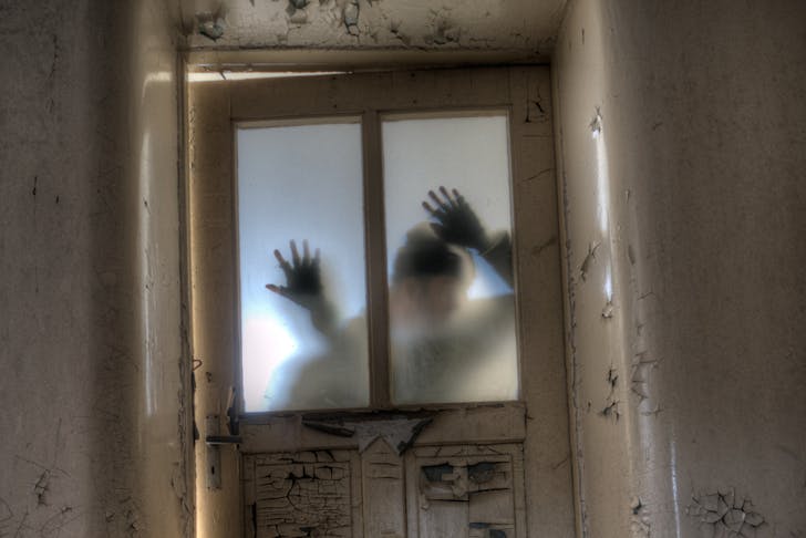 A man's shadow on a locked door with hands on the glass.