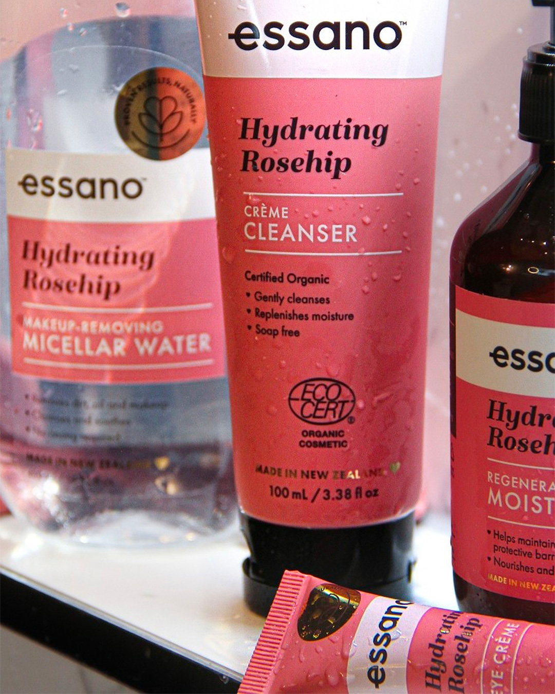 Essano skincare products, including micellar water, cleanser, moisturiser and eye creme, in pink packaging which is covered in water droplets.
