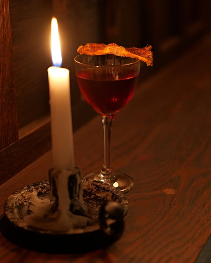 a negroni cocktail pictured beside a burning candle on a bartop for Esteban negroni month
