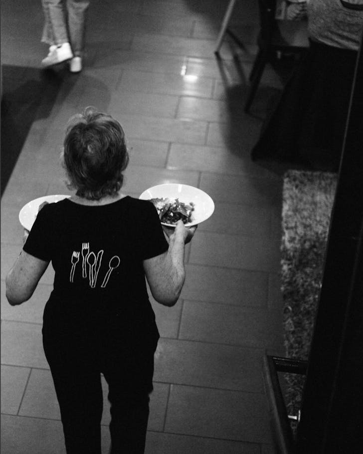 A black and white photo of an Everybody East server carrying two plates.