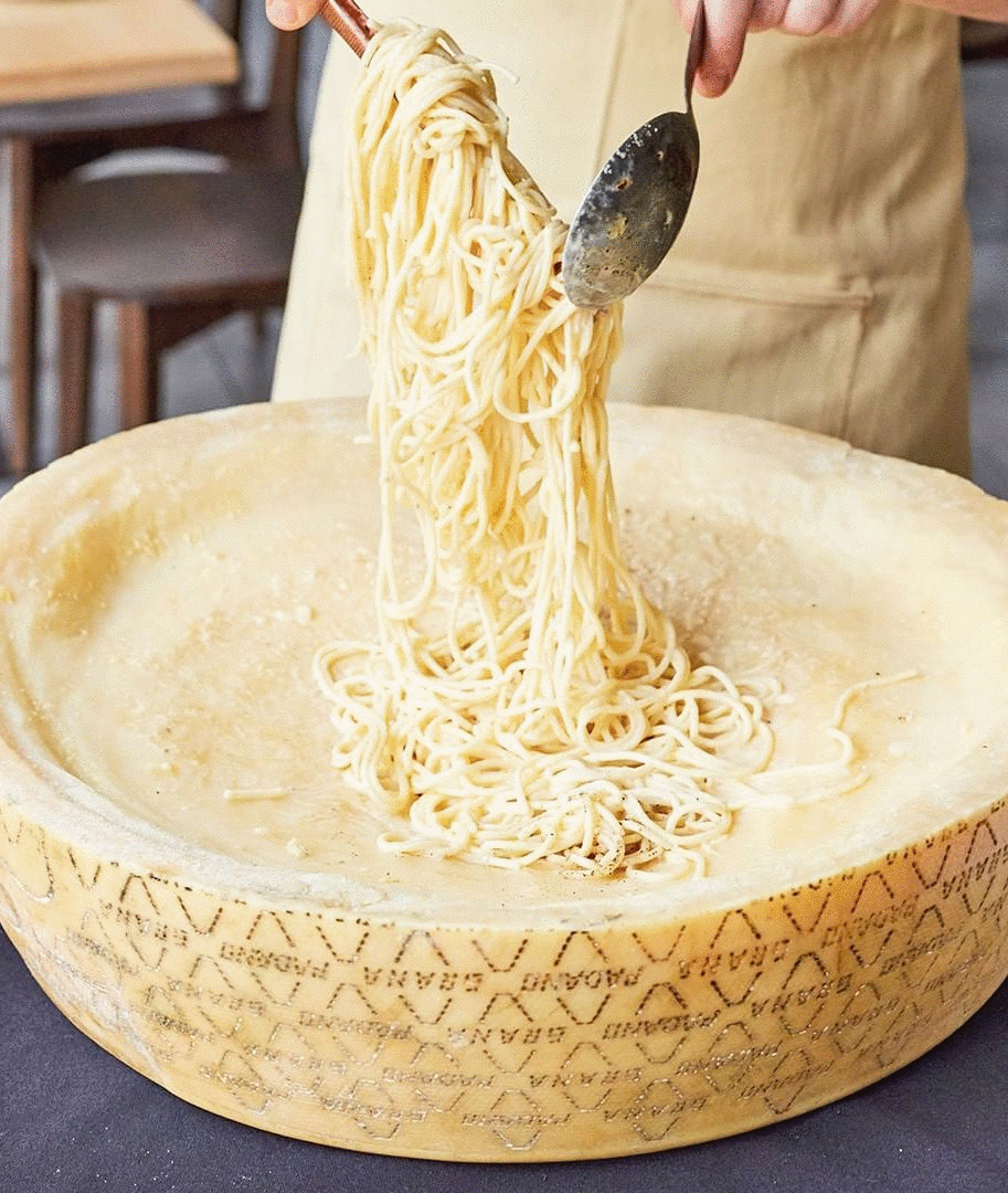 A chef mixes pasta in a wheel of melted cheese.