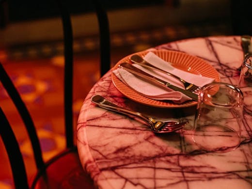 A marble table set with pink plate under a pink neon sign. 