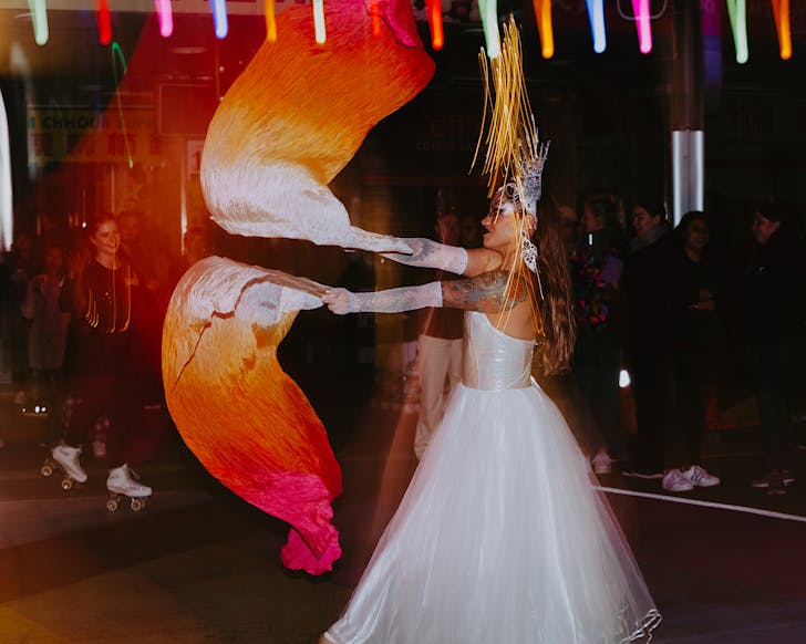 A vibrant street peformer in a customised wedding gown performs in cascading light.