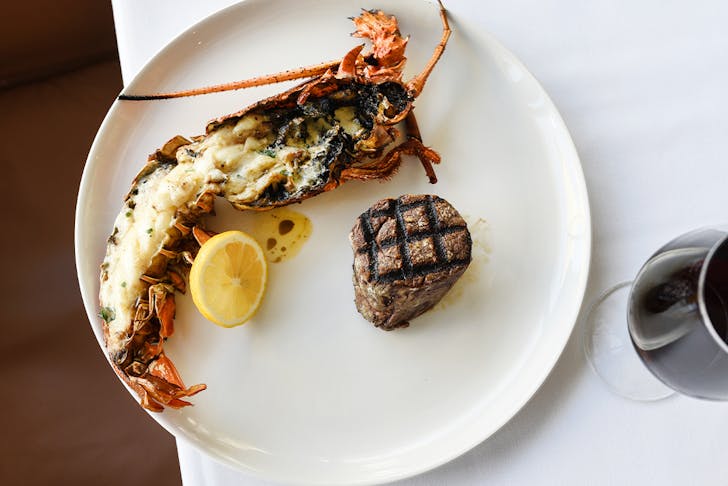 a steak and a half rock lobster on a plate with a glass of wine