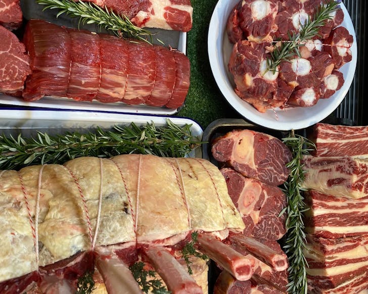 An above view of a variety of butcher meats including ribs. The meat is laid out neatly and there are decorative green leaves across the setup.