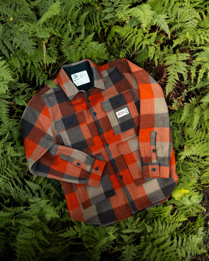 An orange camp jacket lying on a bed of green ferns.